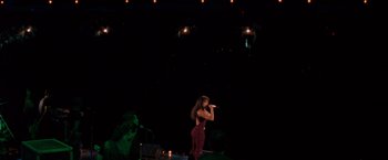 Movie still from “Selena” (1997), directed by Gregory Nava – A woman is singing on a stage with lights in the background; Extreme Wide shot, High angle