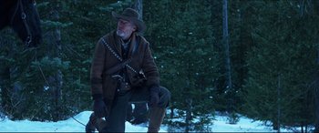 Movie still from “Seraphim Falls” (2006), directed by David Von Ancken – A man in a cowboy hat is kneeling in front of a tree; Medium shot, Low angle