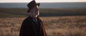 Movie still from “Seraphim Falls” (2006), directed by David Von Ancken – An old man wearing a hat standing in the middle of a field; Medium shot, Low angle