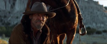 Movie still from “Seraphim Falls” (2006), directed by David Von Ancken – A man with a beard and a cowboy hat sitting in front of a horse; Close Up shot, Over the shoulder angle