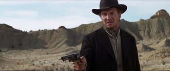 Movie still from “Seraphim Falls” (2006), directed by David Von Ancken – A man holding a gun while wearing a suit and a hat; Close Up shot, Low angle