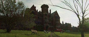 Movie still from “Session 9” (2001), directed by Brad Anderson – An old brick building with a bench in front of it; Extreme Wide shot, Low angle