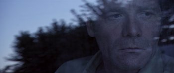 Movie still from “Session 9” (2001), directed by Brad Anderson – A man is looking at the camera through a glass window; Close Up shot, Over the shoulder angle