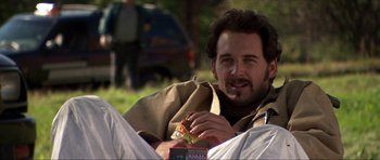 Movie still from “Session 9” (2001), directed by Brad Anderson – A man sitting on the ground eating a piece of pizza; Medium shot, Over the shoulder angle