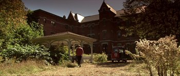 Movie still from “Session 9” (2001), directed by Brad Anderson – A person walking in front of an old red brick building; Extreme Wide shot, Low angle