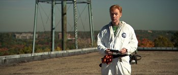 Movie still from “Session 9” (2001), directed by Brad Anderson – A man holding a baseball bat in a field; Medium shot, Over the shoulder angle