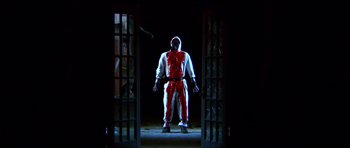 Movie still from “Session 9” (2001), directed by Brad Anderson – A man in a red and white suit standing in a dark room; Wide shot, Low angle