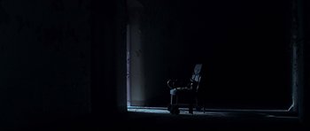 Movie still from “Session 9” (2001), directed by Brad Anderson – A dark room with a person sitting on a chair; Wide shot, Low angle