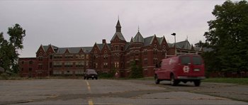 Movie still from “Session 9” (2001), directed by Brad Anderson – A van driving past a large brick building with a clock tower; Extreme Wide shot, Low angle