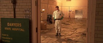 Movie still from “Session 9” (2001), directed by Brad Anderson – A man standing in a room holding a tool; Wide shot, Over the shoulder angle
