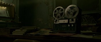 Movie still from “Session 9” (2001), directed by Brad Anderson – An old movie projector sitting on top of a wooden table; Close Up shot, High angle