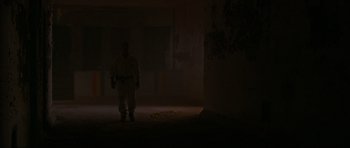 Movie still from “Session 9” (2001), directed by Brad Anderson – A man standing in a dark room holding a gun; Wide shot, Low angle