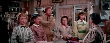 Movie still from “Seven Brides for Seven Brothers” (1954), directed by Stanley Donen – A group of people sitting around a table; Medium shot, Over the shoulder angle