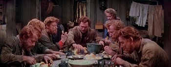 Movie still from “Seven Brides for Seven Brothers” (1954), directed by Stanley Donen – A group of people sitting around a table eating food; Medium shot, High angle