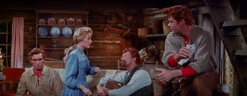 Movie still from “Seven Brides for Seven Brothers” (1954), directed by Stanley Donen – A group of people sitting around a living room together; Medium shot, Low angle