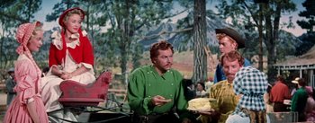 Movie still from “Seven Brides for Seven Brothers” (1954), directed by Stanley Donen – A man in a green shirt is holding a plate of food; Medium shot, Over the shoulder angle