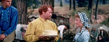 Movie still from “Seven Brides for Seven Brothers” (1954), directed by Stanley Donen – A man in a yellow shirt is holding a plate of food; Medium shot, Over the shoulder angle