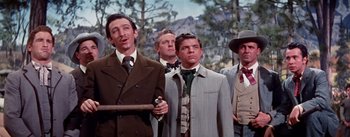 Movie still from “Seven Brides for Seven Brothers” (1954), directed by Stanley Donen – A group of men standing next to each other in suits; Medium shot, Low angle