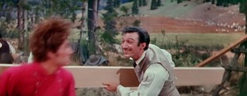 Movie still from “Seven Brides for Seven Brothers” (1954), directed by Stanley Donen – A man holding a piece of wood while wearing a vest; Medium shot, Over the shoulder angle