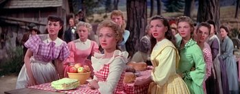 Movie still from “Seven Brides for Seven Brothers” (1954), directed by Stanley Donen – A group of women sitting at a table with food; Medium shot, Low angle