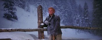 Movie still from “Seven Brides for Seven Brothers” (1954), directed by Stanley Donen – A man standing next to a wooden post in the snow; Medium shot, Low angle