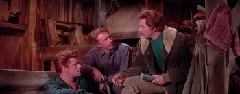 Movie still from “Seven Brides for Seven Brothers” (1954), directed by Stanley Donen – A group of men sitting on the ground talking to each other; Medium shot, Over the shoulder angle