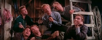Movie still from “Seven Brides for Seven Brothers” (1954), directed by Stanley Donen – A group of men sitting on the ground; Medium shot, Low angle