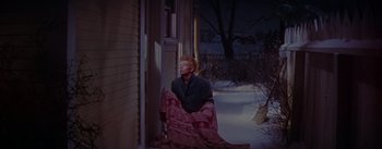 Movie still from “Seven Brides for Seven Brothers” (1954), directed by Stanley Donen – A man sitting on the porch of a house in the snow; Wide shot, High angle
