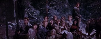 Movie still from “Seven Brides for Seven Brothers” (1954), directed by Stanley Donen – A group of people sitting next to each other in front of a tree; Wide shot, Low angle