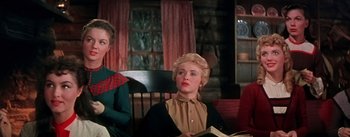 Movie still from “Seven Brides for Seven Brothers” (1954), directed by Stanley Donen – A woman sitting in a chair with a book in her lap; Medium shot, Low angle