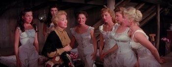 Movie still from “Seven Brides for Seven Brothers” (1954), directed by Stanley Donen – A group of women in white dresses standing next to each other; Medium shot, Low angle