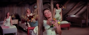 Movie still from “Seven Brides for Seven Brothers” (1954), directed by Stanley Donen – A woman holding a bouquet of flowers in front of two other women; Medium shot, Low angle