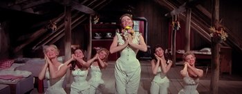 Movie still from “Seven Brides for Seven Brothers” (1954), directed by Stanley Donen – A group of women dressed in white and holding a banana; Medium shot, Low angle