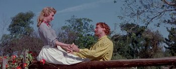 Movie still from “Seven Brides for Seven Brothers” (1954), directed by Stanley Donen – A man and a woman sitting on top of a wooden bench; Medium shot, Low angle