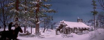 Movie still from “Seven Brides for Seven Brothers” (1954), directed by Stanley Donen – A log cabin in the snow near a pine tree; Extreme Wide shot, Low angle