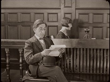 Movie still from “Seven Chances” (1925), directed by Buster Keaton – An older man sitting in front of a judge's bench; Medium shot, High angle