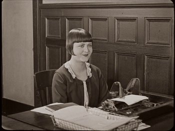 Movie still from “Seven Chances” (1925), directed by Buster Keaton – A woman sitting at a desk in front of a computer; Medium shot, High angle