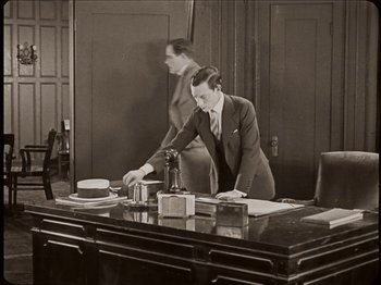 Movie still from “Seven Chances” (1925), directed by Buster Keaton – A man standing at a desk in an office setting; Medium shot, High angle