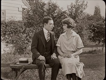 Movie still from “Seven Chances” (1925), directed by Buster Keaton – An old black and white photo of a man and a woman sitting on a bench; Medium shot, Low angle