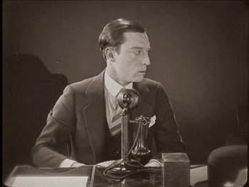 Movie still from “Seven Chances” (1925), directed by Buster Keaton – A man sitting at a table with a phone; Medium shot, High angle