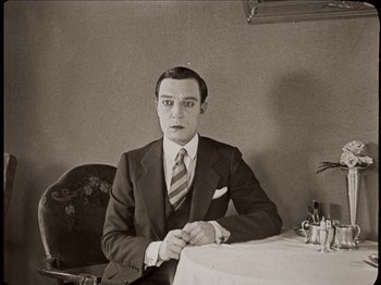 Movie still from “Seven Chances” (1925), directed by Buster Keaton – A man sitting at a table in a suit and tie; Medium shot, High angle