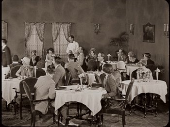 Movie still from “Seven Chances” (1925), directed by Buster Keaton – A group of people sitting at tables in a room; Wide shot, High angle