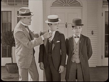 Movie still from “Seven Chances” (1925), directed by Buster Keaton – A man in a suit and a tie and two boys in suits and hats; Medium shot, Low angle