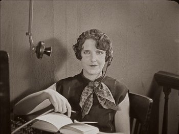 Movie still from “Seven Chances” (1925), directed by Buster Keaton – A woman sitting at a table with a book and a phone; Medium shot, High angle
