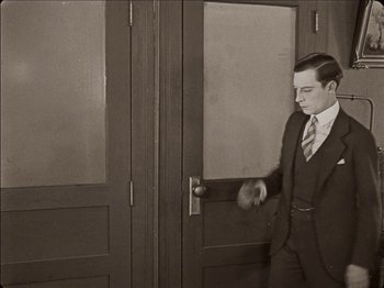 Movie still from “Seven Chances” (1925), directed by Buster Keaton – A man standing in front of a door; Medium shot, Low angle