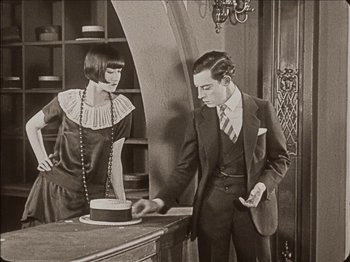 Movie still from “Seven Chances” (1925), directed by Buster Keaton – A man and a woman standing in front of a cake on top of a table; Medium shot, High angle