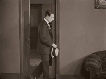 Movie still from “Seven Chances” (1925), directed by Buster Keaton – A black and white photo of a man in a suit holding a hat; Wide shot, High angle