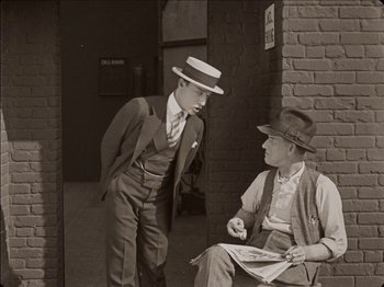 Movie still from “Seven Chances” (1925), directed by Buster Keaton – Two men in suits and hats are sitting on a brick wall; Medium shot, Over the shoulder angle