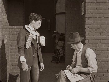 Movie still from “Seven Chances” (1925), directed by Buster Keaton – A young man and an older man are talking in an old photo; Medium shot, High angle