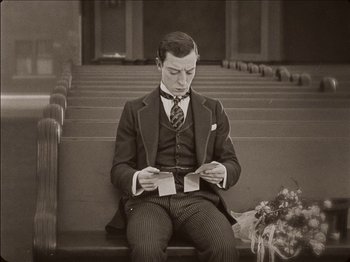 Movie still from “Seven Chances” (1925), directed by Buster Keaton – A black and white photo of a man sitting on a bench; Medium shot, Low angle